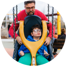 Father pushing son on an adaptive swing