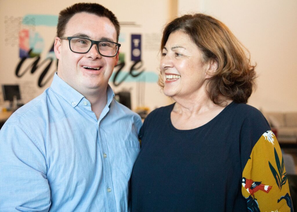 Man in a blue shirt and glasses with Down Syndrome and his female caregiver.