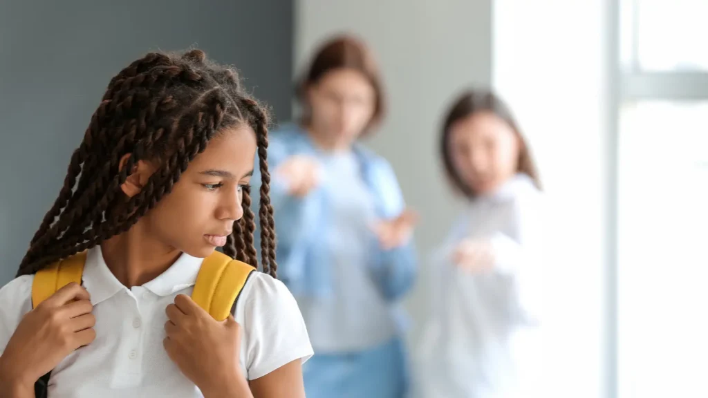 Student looking down while classmates talk behind her.
